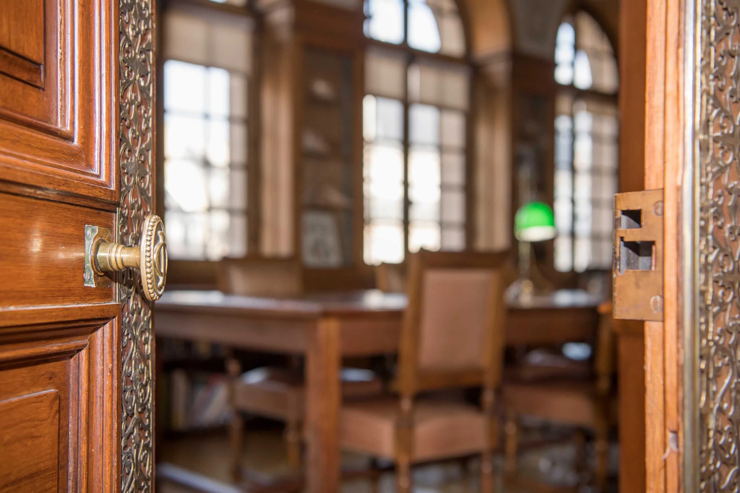 La porte entrouverte de la bibliothèque de l’Institut, sa poignée de laiton ouvragée, et la salle de lecture en arrière-plan.