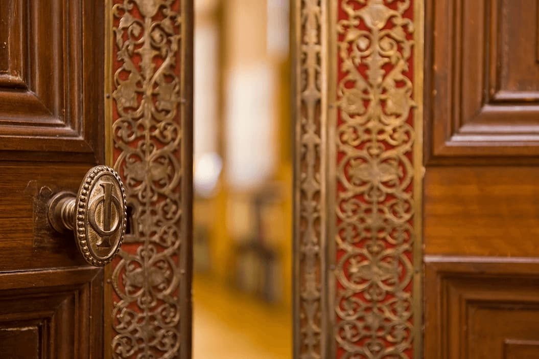 La poignée de porte gravée du monogramme « IO » de l’Institut océanographique, sur les boiseries et les ferronneries dorées d’une porte intérieure.