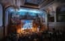 Le grand amphithéâtre en configuration concert, ses fresques baignées d’un éclairage scénique bleu, face à une salle comble.