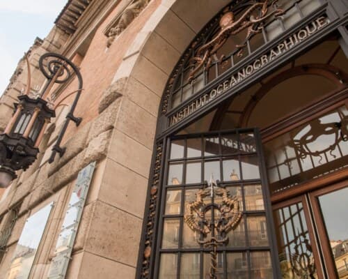 Le porche d'entrée en contre-plongée : arc de pierre sculptée portant l'inscription « Institut océanographique », lanterne de fer forgé et portes vitrées.
