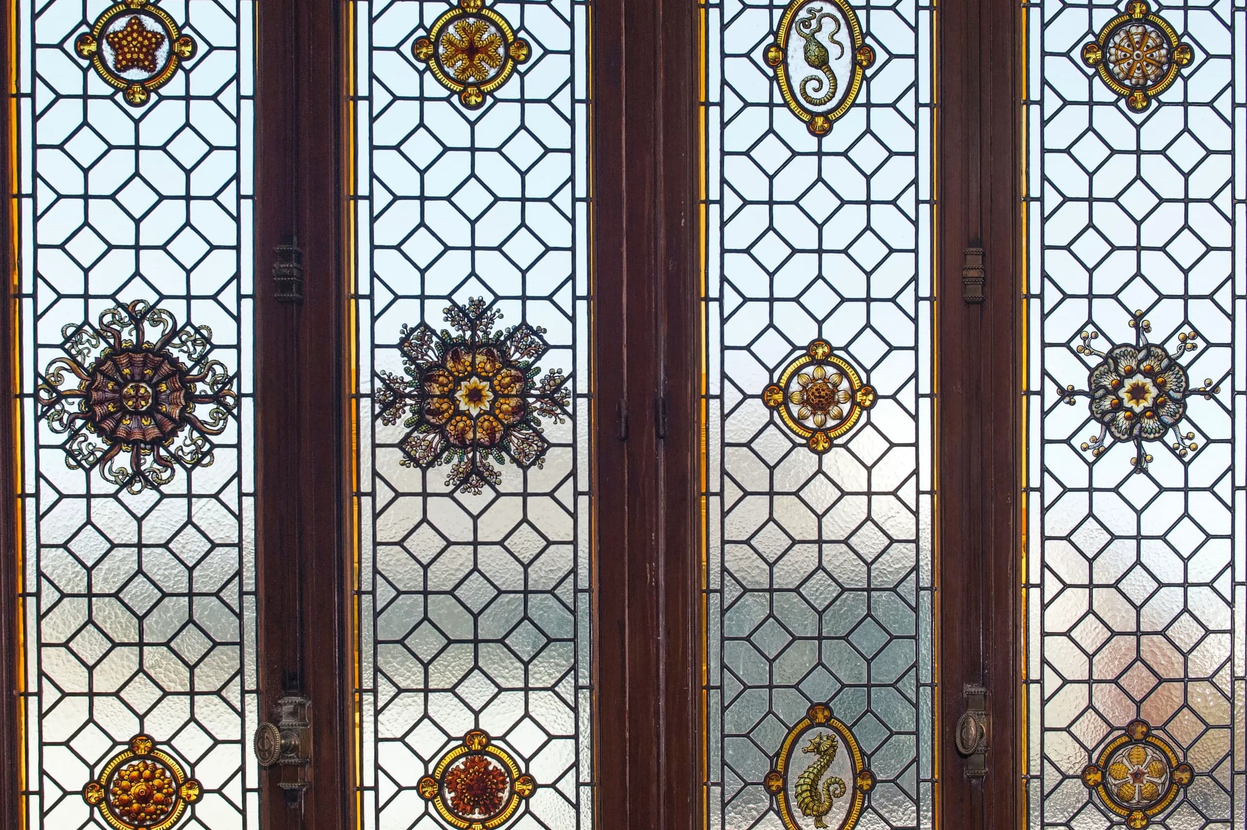 Portes vitrées à petits bois plombés en résille hexagonale, ornées de rosaces de vitrail jaunes et bordeaux.