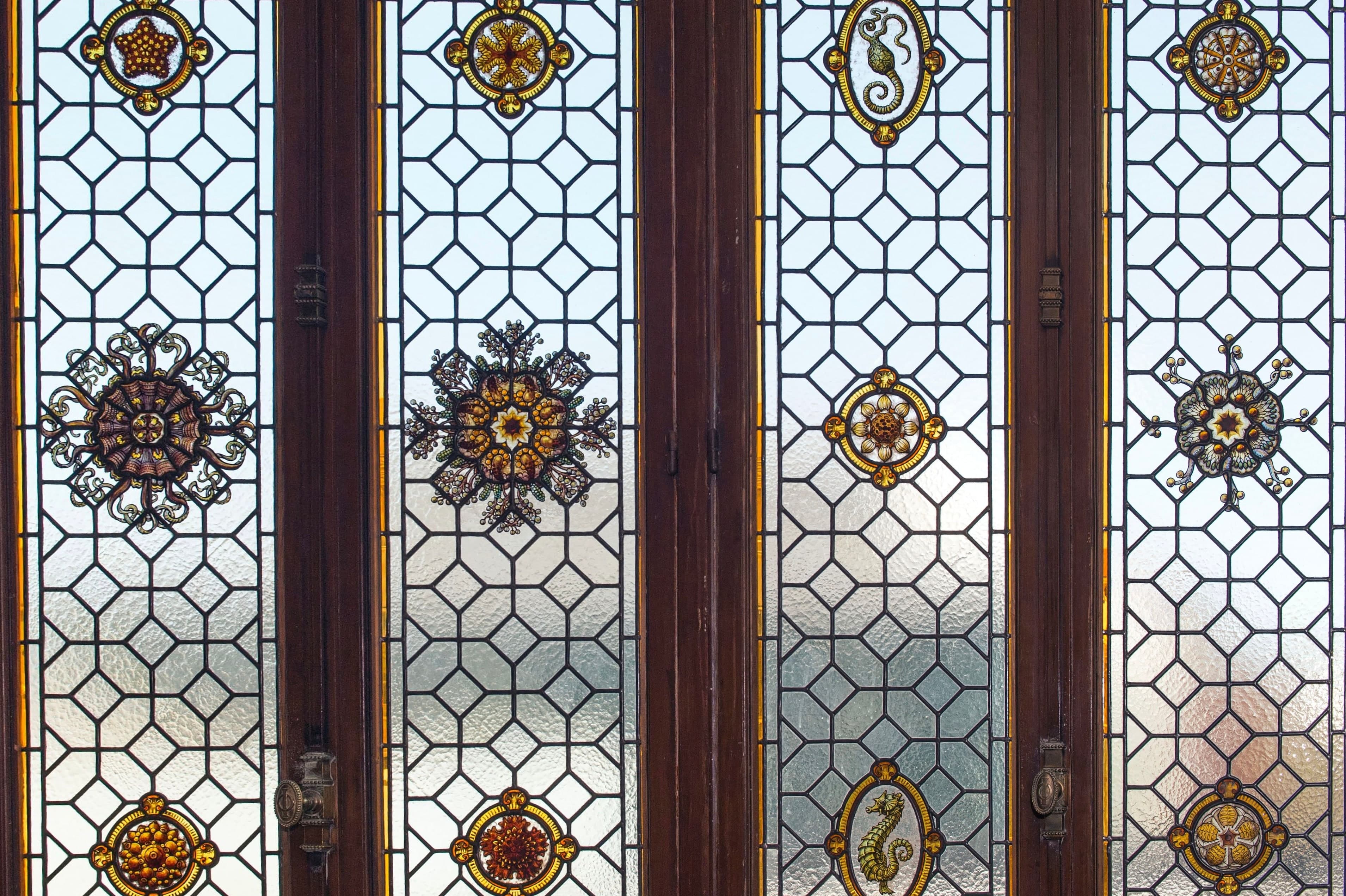 Portes vitrées à petits bois plombés en résille hexagonale, ornées de rosaces de vitrail jaunes et bordeaux.